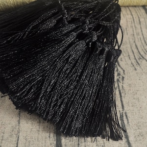 Peut inclure: Un groupe de franges noires, avec une texture soyeuse, est disposé sur une surface brun clair.