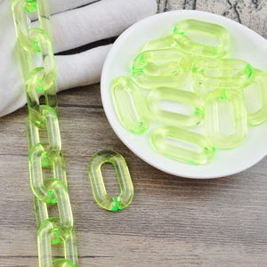 May include: A chain made of bright green plastic links. The chain is lying on a white surface. There is a bowl of bright green plastic links on a wooden surface.