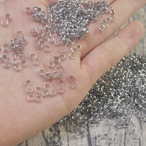 May include: A large pile of silver-toned metal S-shaped hooks. The hooks are small and have a double loop on one end.