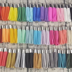 Może przedstawiać: Trzydzieści trzy frędzle w różnych kolorach z srebrnymi metalowymi końcówkami. Frędzle są ułożone w trzech rzędach po jedenaście. Frędzle są wykonane z miękkiego, puszystego materiału.