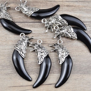Può includere: Sette ciondoli a forma di dente di lupo in argento con pietre di onice nero. I ciondoli sono dettagliati con intricati disegni di testa di lupo in argento.
