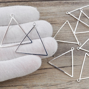 May include: A set of silver triangle-shaped metal earring blanks with jump rings. The blanks are on a white surface.