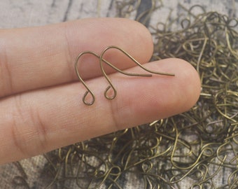 May include: Two gold-toned earring hooks, also known as French hooks, are shown in a close-up image. The hooks are made of metal and have a simple, elegant design.