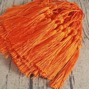 Puede incluir: Un montón de borlas naranjas, atadas juntas, con un nudo en la parte superior. Las borlas están hechas de un material suave y sedoso.