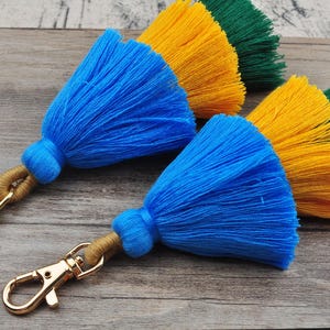 May include: A set of three colorful tassel keychains with gold metal key rings. The tassels are blue, yellow, and green.