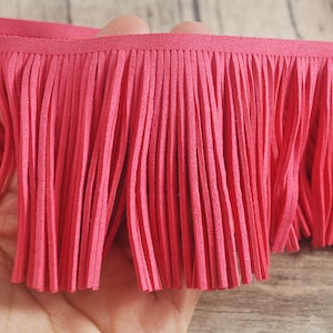 May include: A close-up of a bright pink fringe trim. The fringe is made of soft, thin strands of fabric.