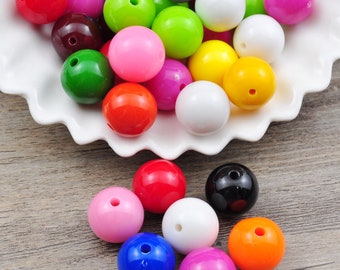 Puede incluir: Un bol lleno de cuentas redondas de plástico de colores brillantes. Las cuentas son de varios colores, incluyendo rojo, verde, azul, amarillo, rosa y blanco. Algunas cuentas están esparcidas sobre una superficie de madera.