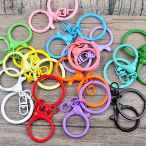 Puede incluir: Surtido de llaveros de metal de colores con cierres giratorios. Los llaveros son de varios colores, incluyendo rojo, naranja, amarillo, verde, azul, morado y rosa.