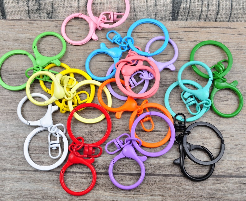 Puede incluir: Surtido de llaveros de metal de colores con cierres giratorios. Los llaveros son de varios colores, incluyendo rojo, naranja, amarillo, verde, azul, morado y rosa.