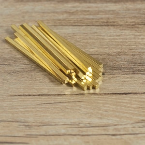 Può includere: Un fascio di aste metalliche quadrate di colore dorato, impilate e disposte a ventaglio. Le aste sono lisce e lucide, con dimensioni e forma uniformi.