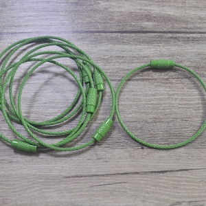 May include: A close-up of two green cable ties. The cable ties are made of a braided metal cable and have green plastic ends.