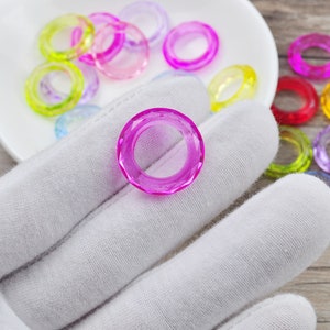 May include: A close-up of a single, bright pink, faceted ring, with a variety of other colorful rings in the background.
