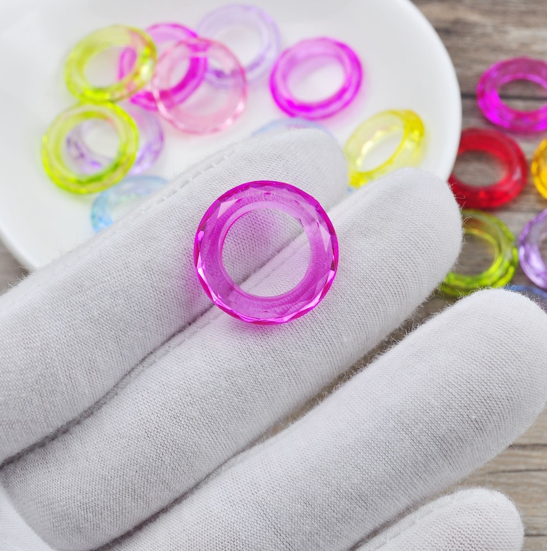 May include: A close-up of a single, bright pink, faceted ring, with a variety of other colorful rings in the background.