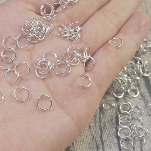 May include: A close-up of a hand holding a large quantity of silver jump rings. The rings are small and circular, and they are ideal for jewellery making.