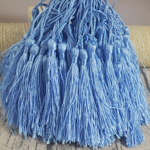Puede incluir: Un montón de borlas de color azul claro, todas atadas juntas. Las borlas están hechas de un material suave y sedoso y tienen aproximadamente 5 cm de largo.