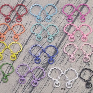 May include: Thirteen pairs of metal keychains in various colors, each shaped like a seashell with a swivel clasp. The keychains are numbered 1 through 13.