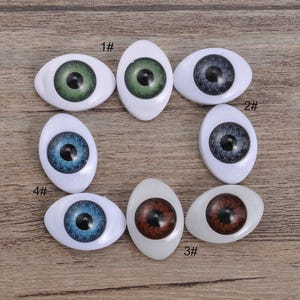 Puede incluir: Un conjunto de ocho ojos de muñeca ovalados de plástico con esclerótica blanca e iris de colores en tonos verde, azul, gris y marrón. Cada ojo presenta una pupila negra y un patrón de iris texturizado. Los artículos están etiquetados con 1#, 2#, 3# y 4#.
