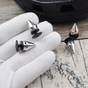 Op de afbeelding: Drie zilveren metalen schoenspikes met zwarte kunststof bases. De spikes zijn puntig en hebben een glanzende afwerking.