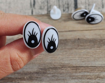 May include: Four white plastic doll eyes with black pupils and eyelashes. The eyes are oval shaped and have a small hole in the back for attaching to a doll or other craft project.