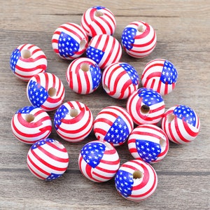 May include: A collection of round wooden beads, each painted with a patriotic design. The beads feature alternating red and white stripes, along with a blue section with white stars, resembling the American flag. The beads are scattered on a wooden surface.