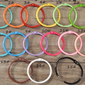 May include: Fifteen colourful binder rings in a range of shades: teal, orange, red, yellow, green, blue, purple, pink, brown, white, and black. Each ring is numbered for identification. Measurements are in centimetres.