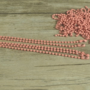 May include: A pile of pink metal chain with a few strands laid out on a wooden surface. The chain is made of small, round links.
