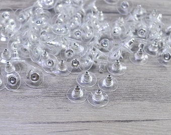 May include: A large pile of clear plastic earring backs with silver metal posts. The backs are designed to be used with stud earrings.