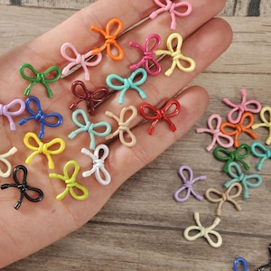 Könnte beinhalten: Eine Sammlung kleiner, farbenfroher Schleifenverzierungen in verschiedenen Farbtönen, darunter Rosa, Orange, Grün und Blau. Die Schleifen sind auf einer Hand und einer Holzoberfläche verteilt und bieten ein Bastelthema.