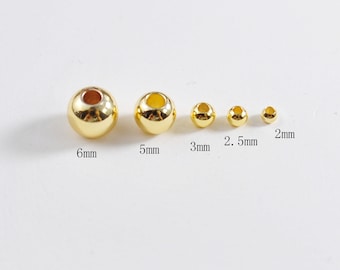 May include: A set of six gold-colored metal beads in various sizes, ranging from 2 mm to 6 mm. The beads are arranged in order of size, with the largest bead on the left and the smallest bead on the right. The beads are all round and have a smooth surface.