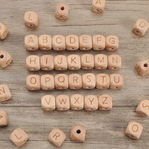 May include: Wooden alphabet beads with letters A to Z, in various sizes and orientations. The beads are light brown with a natural wood grain. Some beads have holes for stringing.