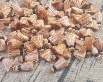 May include: A large pile of small, brown and white tassels with gold metal rings. The tassels are made of a soft, fluffy material and are perfect for adding a touch of whimsy to any project.
