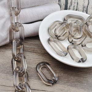 May include: A close-up of a chain made of clear plastic links. The chain is lying on a wooden surface. There is a pile of clear plastic links on a white plate.