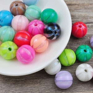 Può includere: Una collezione di perline rotonde di plastica colorate, striate e con una finitura scintillante. Le perline sono disposte su un piatto bianco e una superficie di legno.