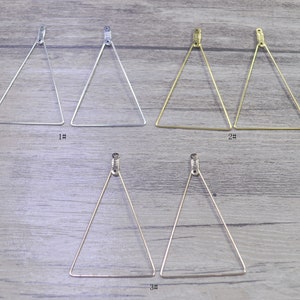 May include: Three pairs of triangle-shaped earring hoops. The first pair is silver, the second pair is gold, and the third pair is silver. Each pair is shown on a wooden surface.
