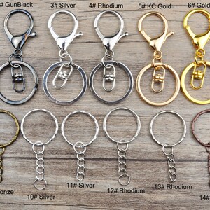 May include: Assortment of 15 keychains in various finishes, including bronze, gun black, silver, rhodium, gold, and copper. Each keychain features a circular ring and a swivel clasp. Some keychains also include a chain.
