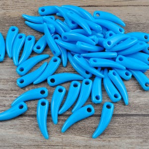 May include: A large group of blue plastic horn-shaped beads with a hole at the top. The beads are scattered on a wooden surface.