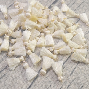 May include: A pile of off-white tassel trim with gold metal rings. The tassels are made of soft, fluffy yarn.