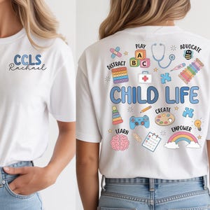 May include: White t-shirt with "CCLS Rachael" in blue script on the front. The back features the words "CHILD LIFE" in blue, surrounded by colorful illustrations of toys, medical tools, and educational elements.