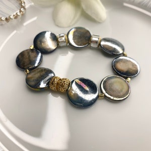 May include: A bracelet made of iridescent gray round beads with gold accents. The bracelet has a simple design and is perfect for everyday wear.