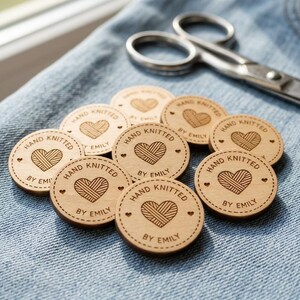 May include: A collection of round, light-colored wooden tags featuring a laser-engraved design of a heart made of yarn. Each tag is inscribed with the text "HAND KNITTED BY EMILY" and includes small heart accents along the circular border.