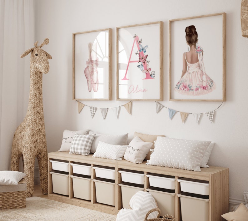 Chambre d'enfant décorée avec trois cadres accrochés au mur représentant des pointes de ballet, une lettre 'A' ornée de papillons et une danseuse de dos en robe fleurie