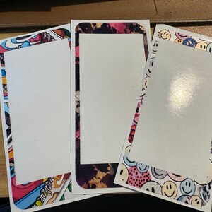 May include: Three rectangular stickers with white centers and colorful borders. One has a border with a mix of patterns and colors, another has a dark, abstract pattern, and the third features smiley faces.