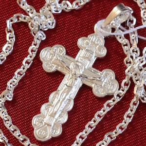 May include: A silver chain necklace with a detailed silver cross pendant. The cross features a figure of Jesus Christ on the front.