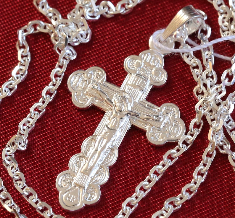May include: A silver chain necklace with a detailed silver cross pendant. The cross features a figure of Jesus Christ on the front.
