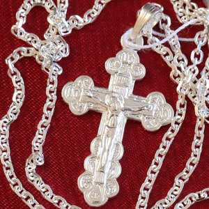 May include: A silver chain necklace with a silver cross pendant. The cross features an ornate design with a figure of Jesus Christ.