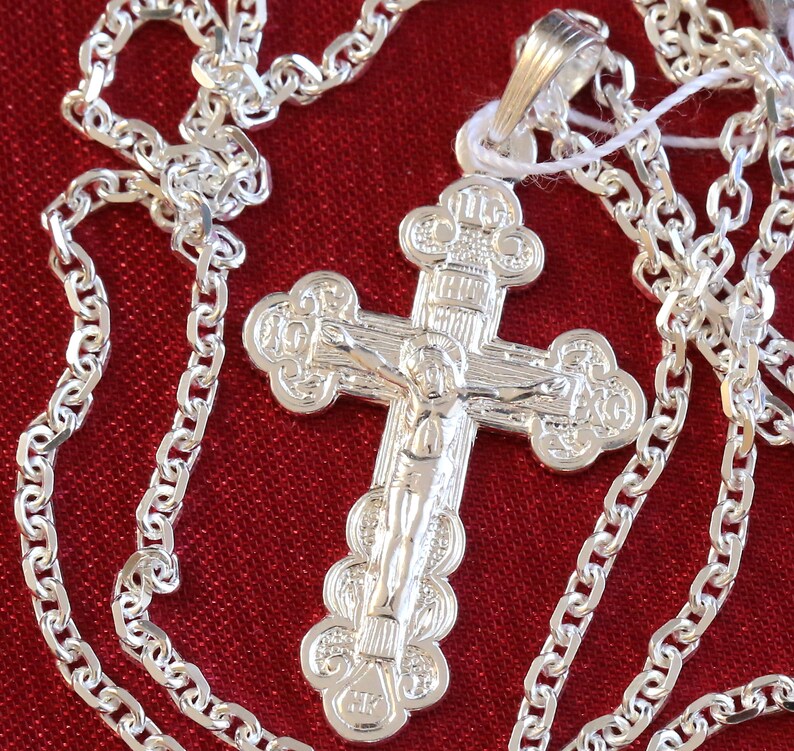 May include: A silver chain necklace with a silver cross pendant. The cross features an ornate design with a figure of Jesus Christ.