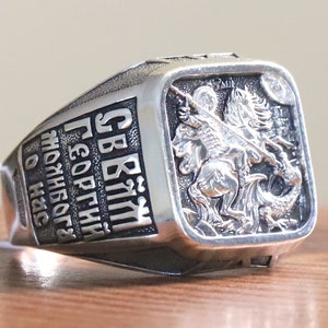 Peut inclure: Une bague en argent avec un visage carré représentant Saint-Georges terrassant un dragon. L'inscription sur le bord est "СВ. ГЕОРГИЙ ПОБЕДИТЕЛЬ ЗЛОГО НАС".