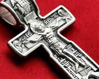 May include: Detailed silver pendant in the shape of a cross, featuring a depiction of Jesus Christ on the cross. The pendant has intricate engravings and religious iconography, with a loop at the top for a chain. The background is a solid red.