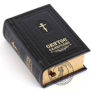 Pu&ograve; includere: Un libro rilegato in pelle nera con lettere dorate che recitano "Святое Евангелие" (Vangelo Santo). Il libro ha una croce dorata sulla copertina anteriore e un segnalibro dorato.