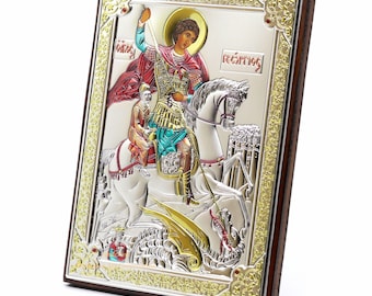 May include: Silver-plated icon of Saint George slaying a dragon, with a gold-colored background and ornate frame. The icon is mounted on a wooden plaque.